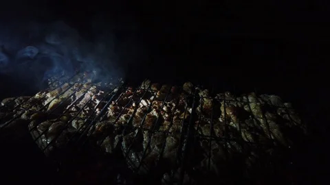 In the dark, meat is grilled on the grill in the rays of a flashlight. Vídeos de archivo 115898543