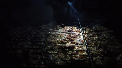 In the dark, meat is grilled on the grill in the rays of a flashlight. 動画素材 115898906