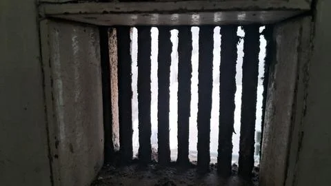 Dark metal bars inside a weathered rectangular stone ventilation shaft opening Stock Photos