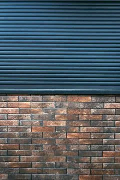 Dark metal roller shutter above a textured brick wall, contrasting horizont.. Fotos Stock