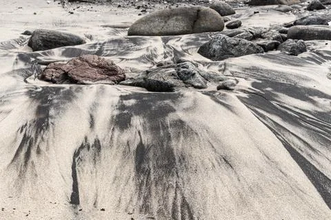 Dark mineral patterns in the beach sand amidst rocks Stock Photos
