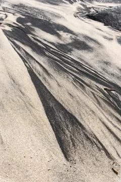 Dark mineral patterns in the beach sand amidst rocks Stock Photos