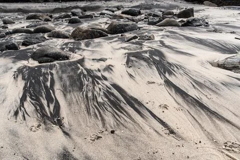 Dark mineral patterns in the beach sand amidst rocks Stock Photos