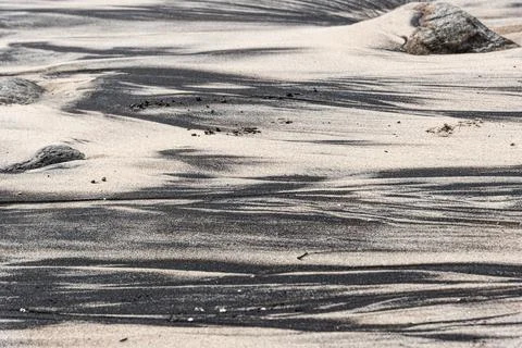 Dark mineral patterns in the beach sand amidst rocks Stock Photos
