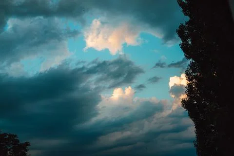 A dark, moody clouds with hints of blue sky and silhouetted tree. Dramatic sky Stock Photos