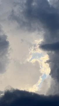 Dark moody storm clouds framing a central glowing opening where bright sunlight Stock Photos