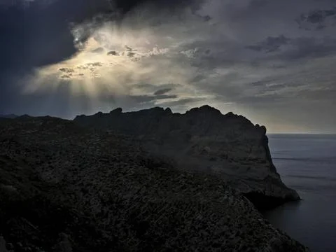 Dark mountain cliffs under cloudy sky with sun rays Stock Photos