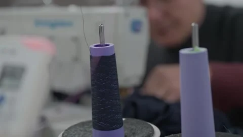 Dark Navy Thread Cones on Sewing Machine Pins with Worker in Background 스톡 동영상 332948792