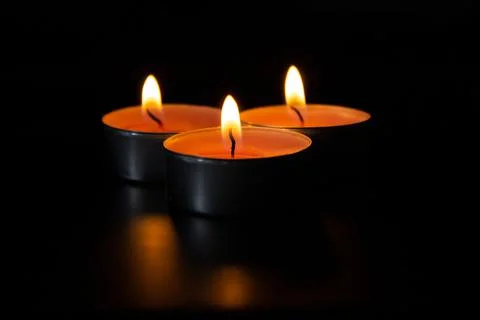 Dark night background, composition of three candles. Black table, side view. Stock Photos