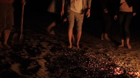 On a dark night in the light of a campfire, man prepares to pass over the embers Stock Footage 115929605