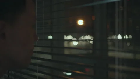 In the dark at night through the blinds, a man follows the street, blurred Stock Footage 156298745