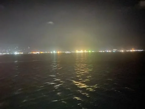 Dark ocean surface at night distant harbor city lights reflection Stock Photos