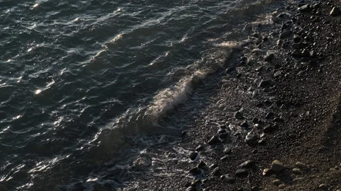 Dark ocean water with gentle waves crashing onto a rocky Stock Footage 331194474
