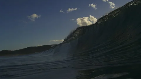Dark Ocean Wave Rising Against Blue Sky and Sunlit Clouds Stock Footage 344033556