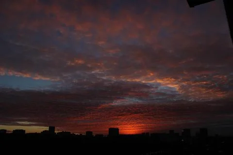 A dark orange sunset that illuminates the clouds flying by over the already nigh Stock Photos