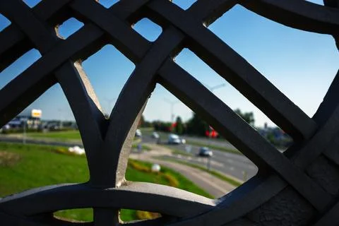Dark ornate metal pattern framing blurred city traffic under blue sky Stock Photos