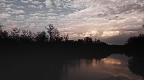 Dark park with a river on the back of a blue sky with small white clouds view Stock Footage 125930677