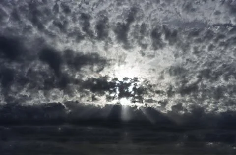 Dark patterned cloudy sky with beaming sun through the clouds Stock Photos