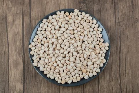 A dark plate full of dried raw white peas on a wooden table Stock Photos