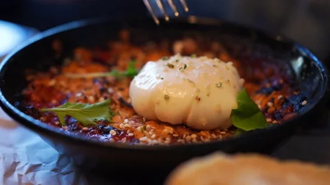 Dark plate hot dish egg lies on top, person cuts egg with knife, holds with fork Stock Footage 138037221