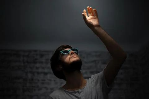 Dark portrait of young guy, looking up and touching the light.  Stock Photos