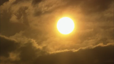 Dark puffy clouds moving over the bright orange sun at sunset, Close up of sun Stock Footage 109437799