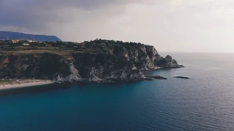 Dark rain cloud over rough rocky cape and turquoise sea waters. Aerial shot of Stock Footage 99002982