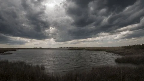 Dark rain clouds passing over a bay and marsh Vidéo 129606722