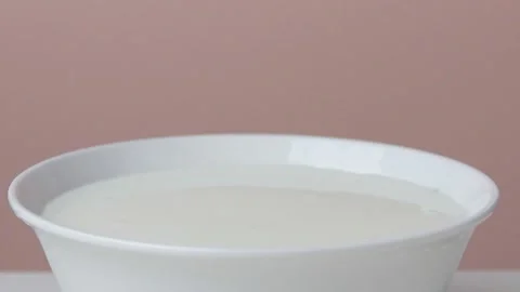 A dark red cherry is falling into a plate of sour cream Stock Footage 135578244