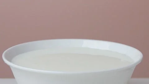 A dark red cherry is falling into a plate of sour cream in slow motion Stock Footage 135578283