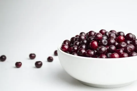 Dark red cherry in a white cup on a white background. And scattered cherries Stock Photos