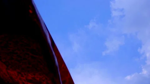 Dark red parasol flutters in the wind against blue sky with tiny clouds Video stock 134909192