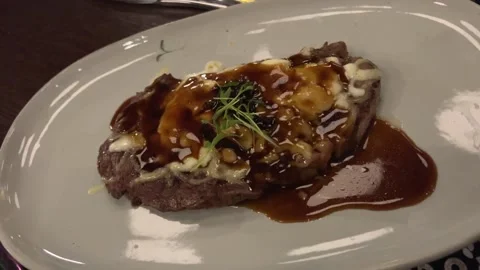 In a dark restaurant at night, a medium rare steak with sauce on a white plate Stock Footage 292972679