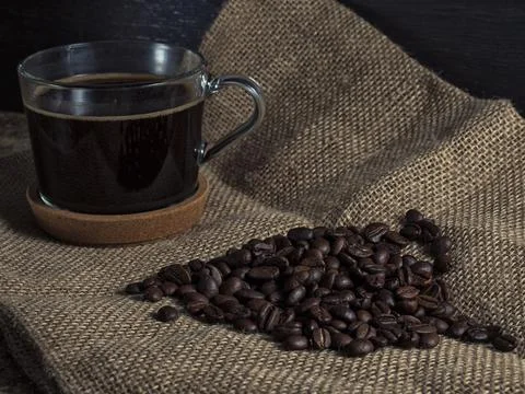Dark roasted coffee beans on burlap and a mug of freshly brewed natural coffee Stock Photos