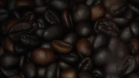 Dark roasted coffee beans fall onto a pile of coffee beans. Stock Footage 301674405