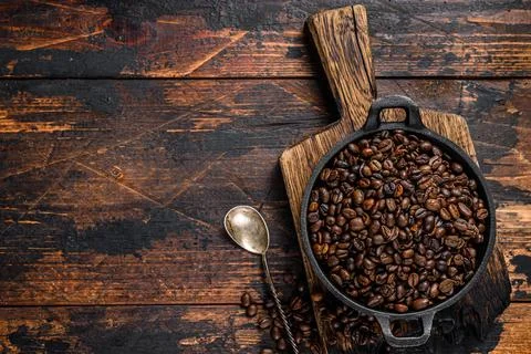 Dark roasted Coffee beans in a pan. Dark wooden background. Top view. Copy space Stock Photos