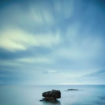 Dark rocks in a blue ocean under cloudy sky in a bad weather. Stock Photos
