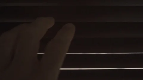 In a dark room a hand opens a crack in the window blinds to peek outside Stock Footage 109164004