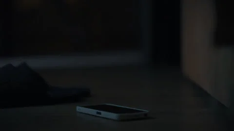 Dark room with a smartphone resting on the floor and shoes in the background Stock Footage 323764566