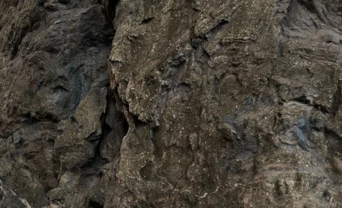 Dark, rough rock face texture.  Close-up view of a craggy, uneven surface Stock Photos