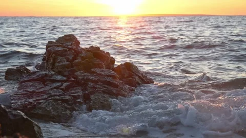 Dark rugged rock formation withstands crashing waves during a golden sunset Stock Footage 337411745