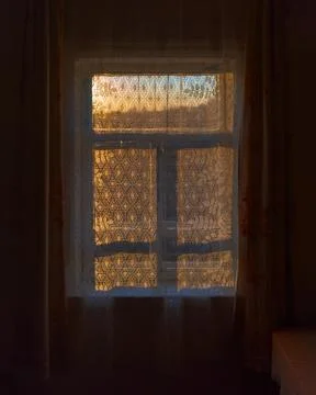 A dark, rustic room with a corner table and a window behind a curtain. Stock Photos
