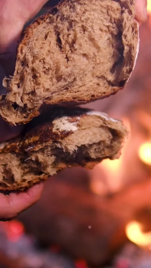 Dark Rye Bread Broken by Male Hands Beside Open Fire at Night with Glowing Stock Footage 345169481