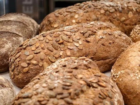 Dark rye bread covered with pumpkin seeds displayed in a bakery, showcasing.. Stock Photos