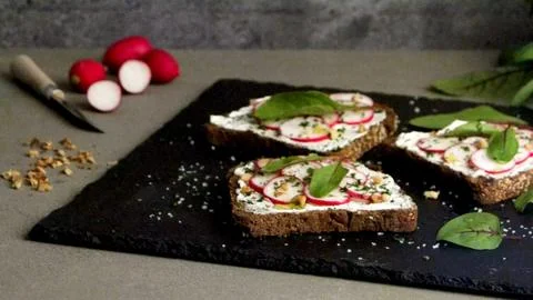 Dark rye bread toasts topped with cream cheese, sliced radishes, and herbs Stock Photos