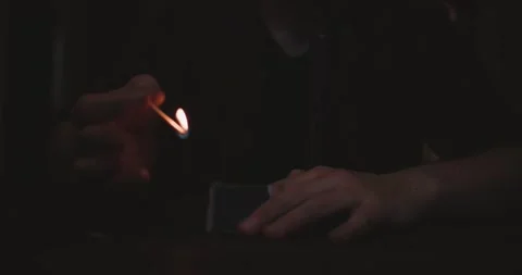 Dark scene with hands of unrecognizable man ignite's match before fire on candle Stock Footage 162500707
