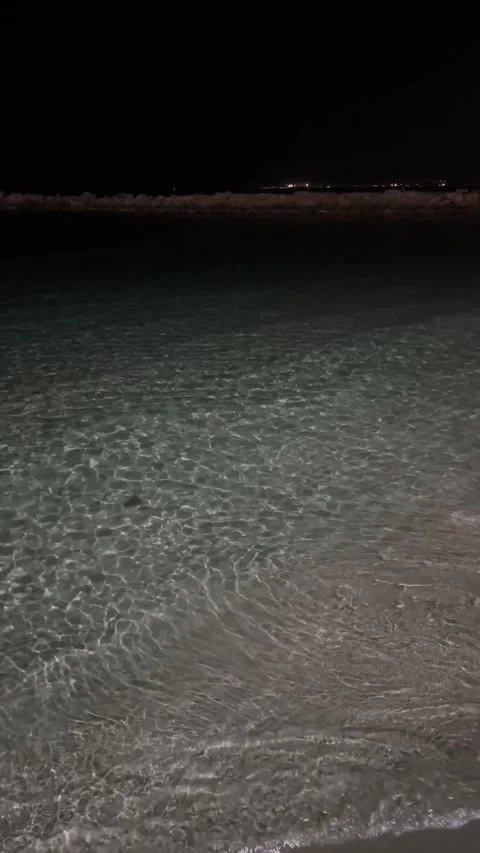 Dark sea water surface at night with gentle ripples and distant city lights 库存影片 338321433
