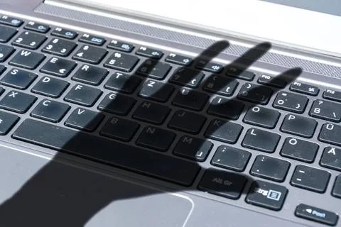 Dark shadow of a hand reaches for computer keyboard symbolizing cyber crim... 写真素材