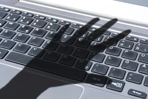 Dark shadow of a hand reaches for computer keyboard symbolizing cyber crime 写真素材