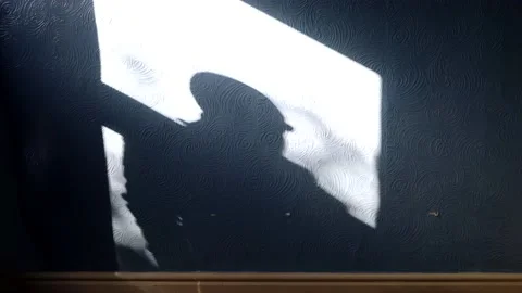 A dark shadow of a man looking through a window with the sun coming through t Stock Footage 219965249